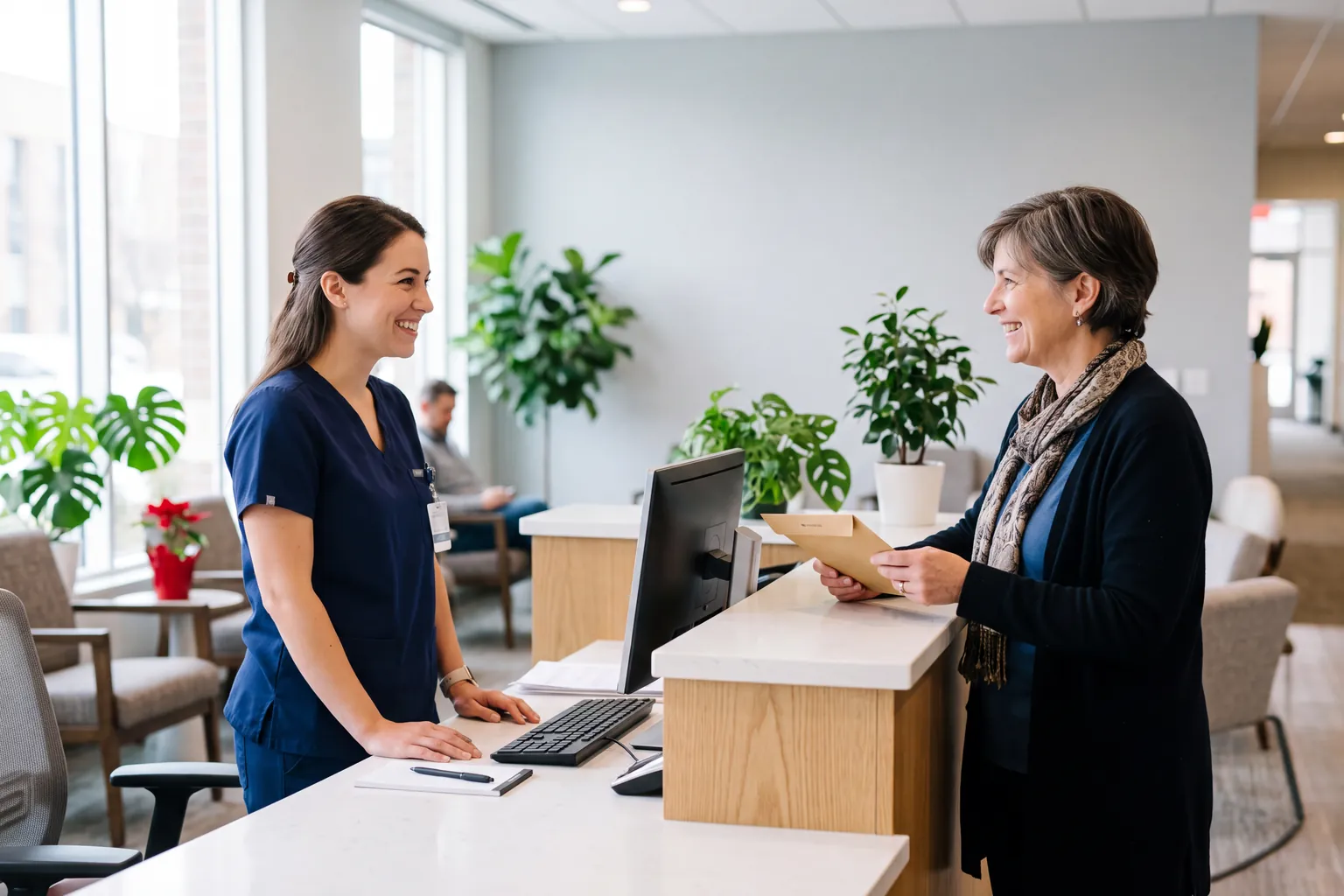 Research clinic coordinator in navy scrubs greeting a woman holding a referral envelope at the front desk